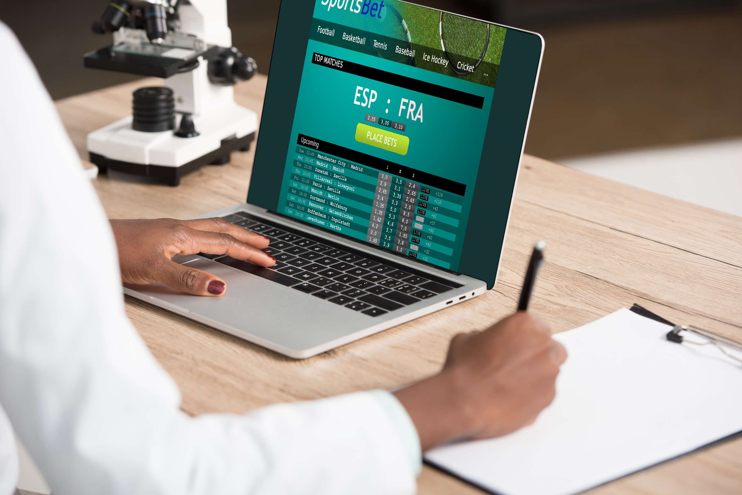 cropped view of african american doctor using laptop with sports bet website near microscope