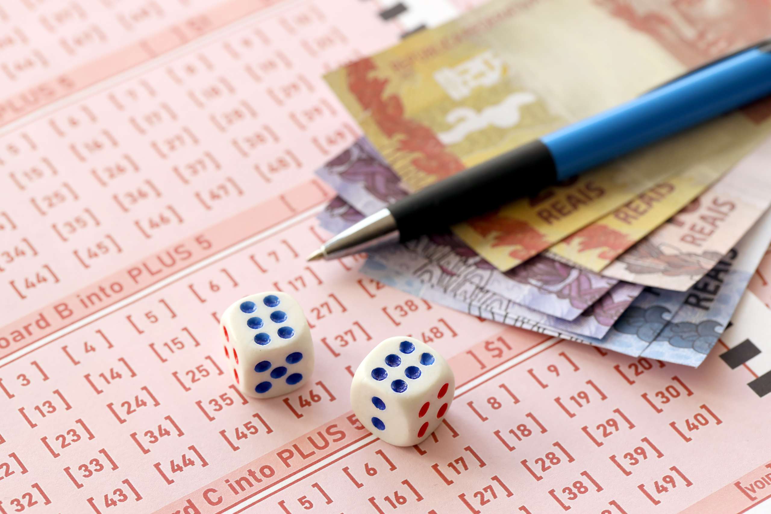 Small dice cubes with Brazilian money bills and pen on blank of lottery game. Concept of luck and gambling in Brazil