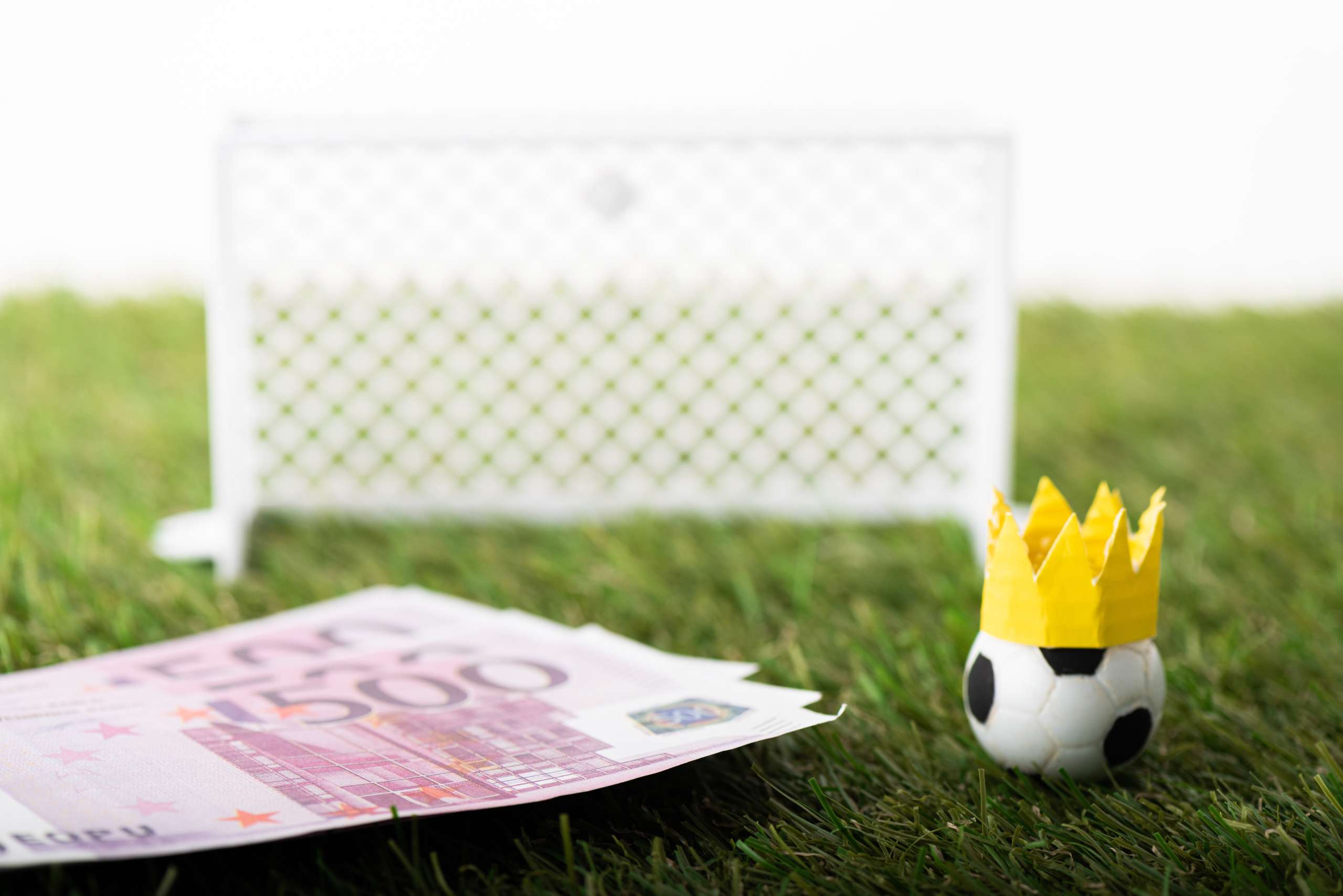 selective focus of toy soccer ball with paper crown near euro banknotes and miniature gates isolated