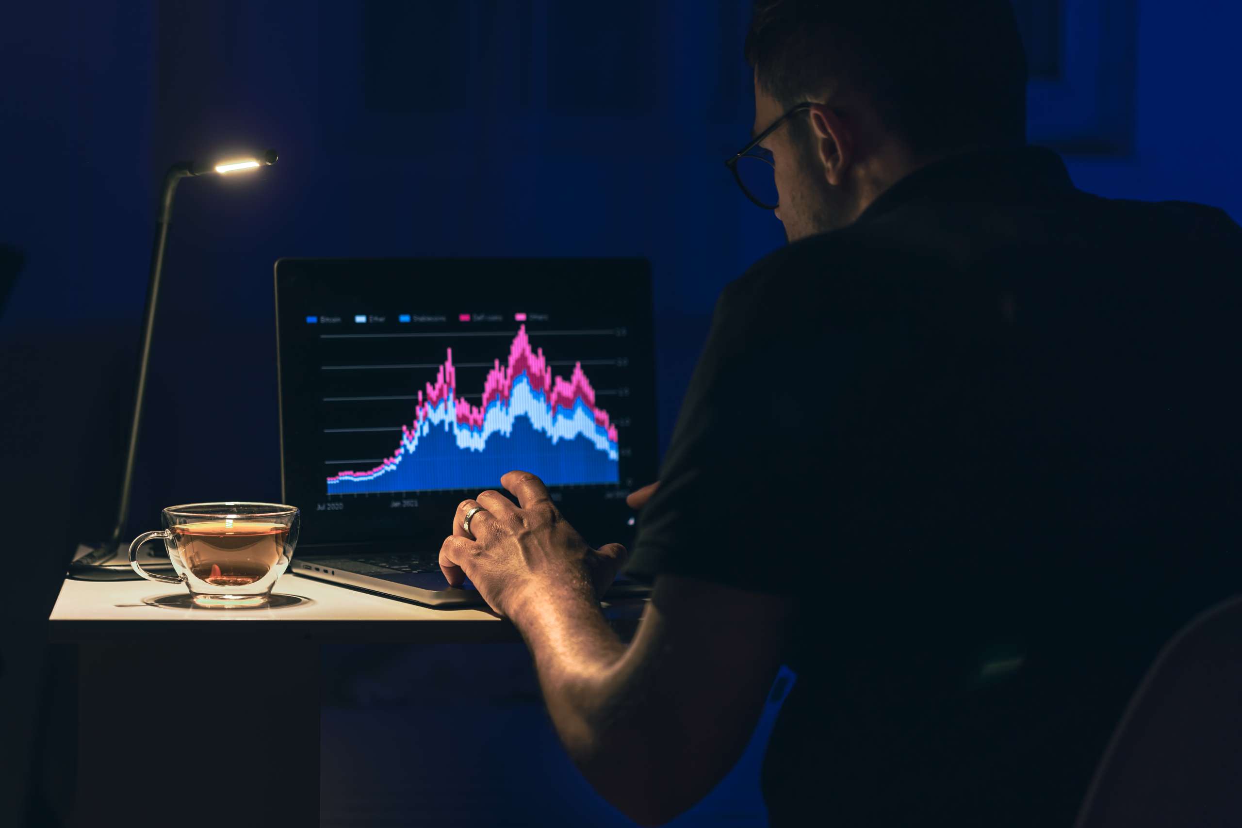 Man trading, browsing online stock investments at night. A man sits in front of a laptop with a chart. Business man stock exchange trader looking at laptop screen.